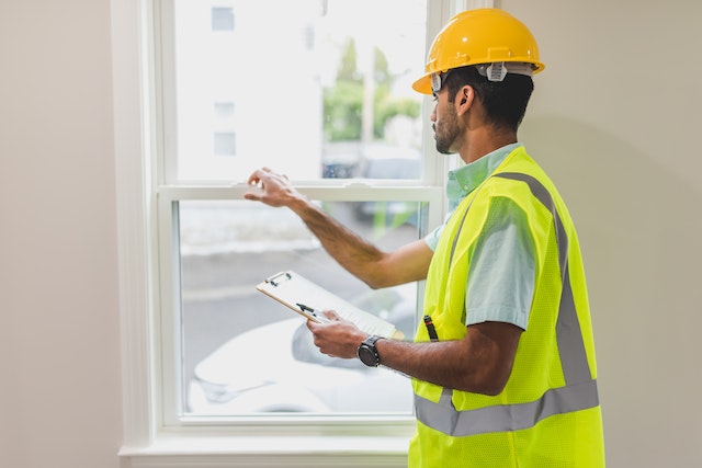 property inspector in hardhat and yellow vest inspecting a window